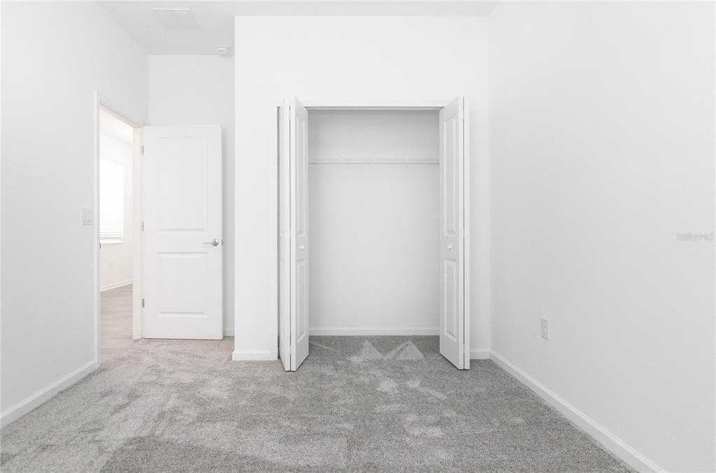 A bedroom with white walls, gray carpet, a closet with bifold doors, and an open doorway — 6346 LIMBERPINE ALLEY, ST CLOUD, FL