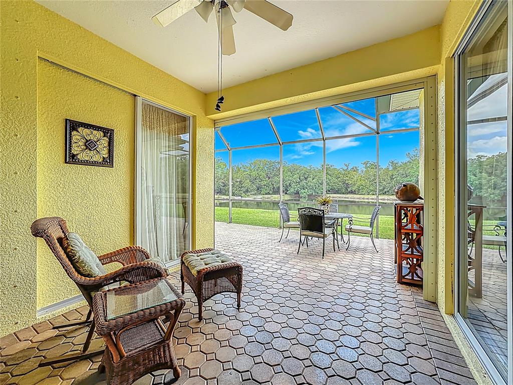 A covered patio with wicker furniture overlooks a lake through a screened-in enclosure — 8721 STONE HARBOUR LOOP, BRADENTON, FL