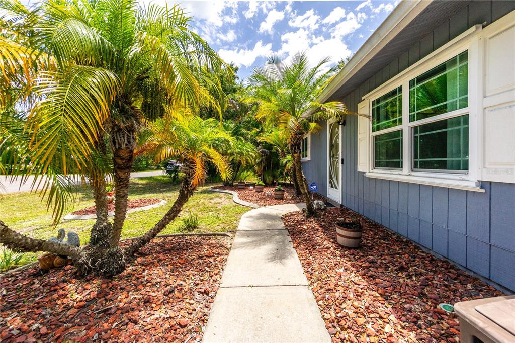 A concrete walkway leads to the front door of a blue house with palm trees — 9435 BREWTON AVENUE, ENGLEWOOD, FL