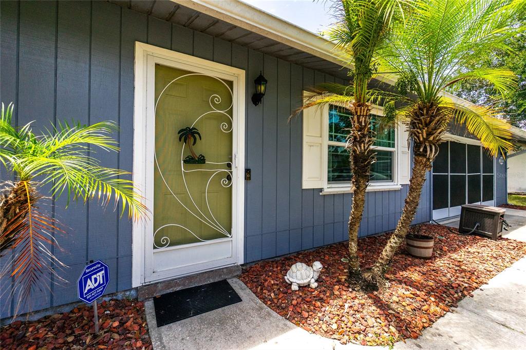The exterior of a house features blue vertical siding, a front door with a decorative screen, and palm trees — 9435 BREWTON AVENUE, ENGLEWOOD, FL