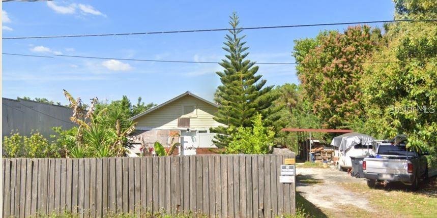 A wooden fence stands in front of a house with a tall pine tree — 6044 ADAMSVILLE ROAD, GIBSONTON, FL