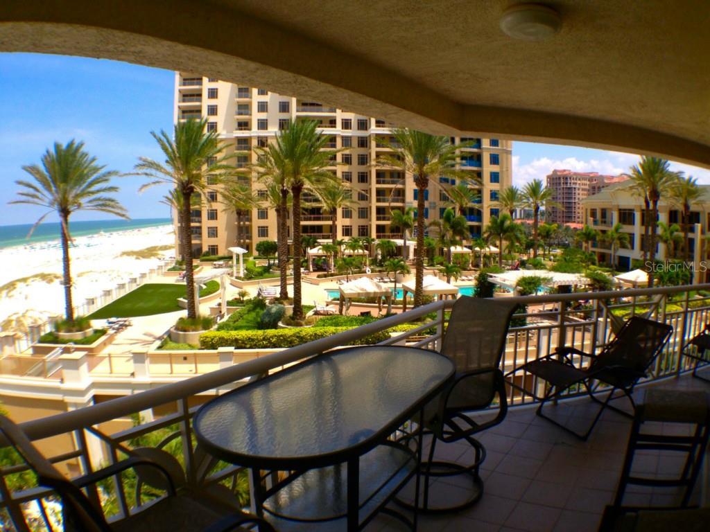 A balcony with patio furniture overlooks a swimming pool, palm trees, and a sandy beach — 11 SAN MARCO STREET UNIT 504, CLEARWATER BEACH, FL