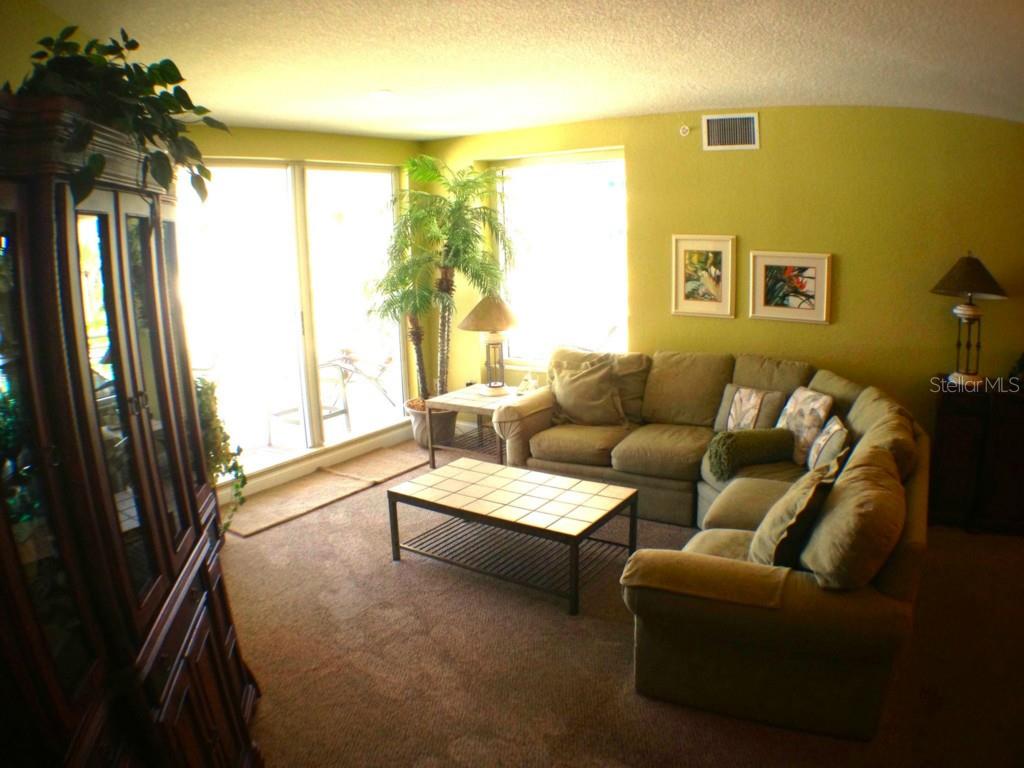 A living room with a sectional sofa, tile-top coffee table, and large windows with plants — 11 SAN MARCO STREET UNIT 504, CLEARWATER BEACH, FL
