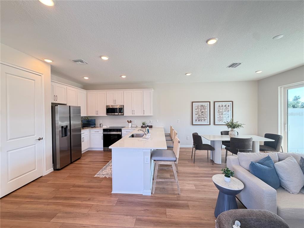 A modern open-concept kitchen and living area with white cabinetry, stainless appliances, and wood flooring — 5839 ANGELA LEYLA PLACE, RIVERVIEW, FL
