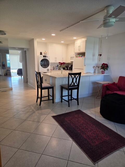 A kitchen with white cabinets and a breakfast bar overlooks a tiled living area — 460 Horizons W # 111, Boynton Beach FL 33435, BOYNTON BEACH, FL