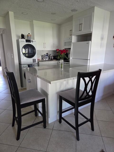 A kitchen features white cabinets, a stacked washer-dryer, a stone island, and two bar stools — 460 Horizons W # 111, Boynton Beach FL 33435, BOYNTON BEACH, FL