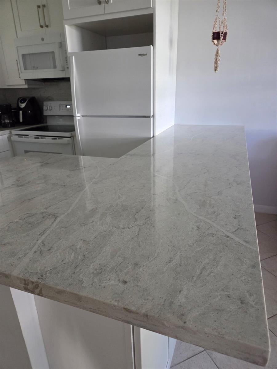 A kitchen features a white refrigerator, white cabinetry, and a light-colored stone countertop peninsula — 460 Horizons W # 111, Boynton Beach FL 33435, BOYNTON BEACH, FL