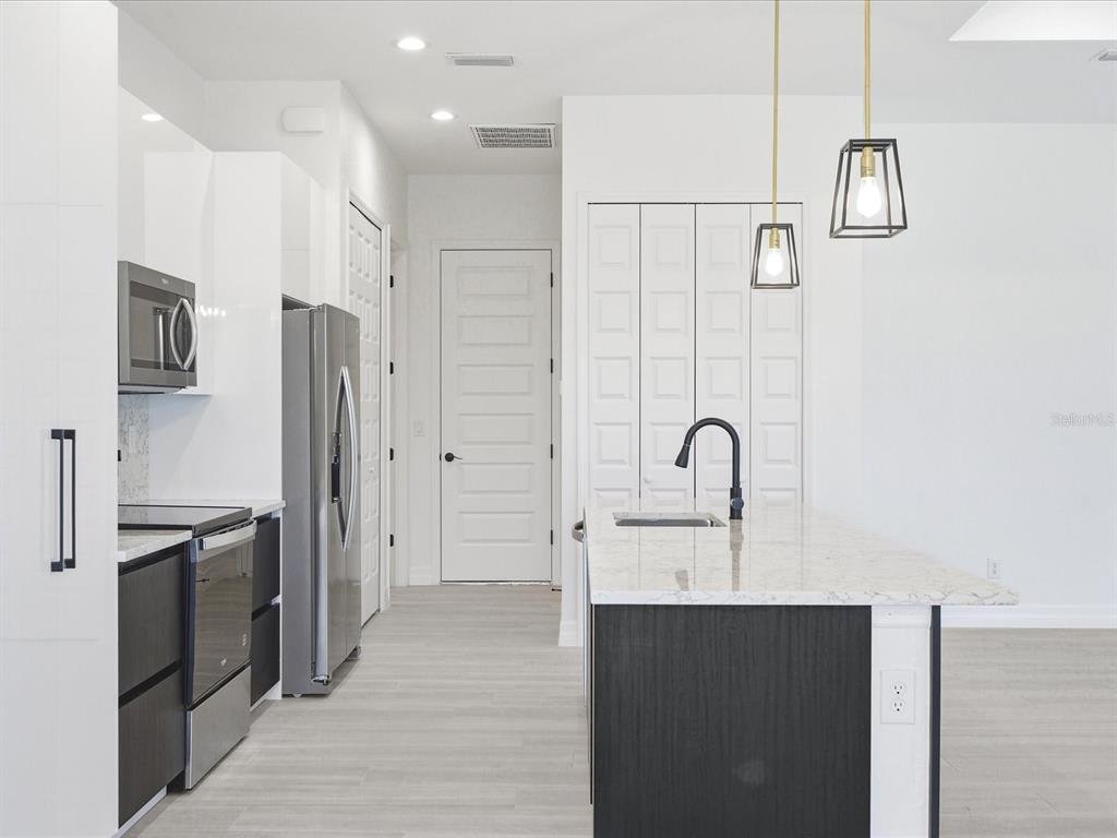 A modern kitchen features a white island, dark cabinetry, stainless steel appliances, and pendant lighting — 72 TEE VIEW ROAD, ROTONDA WEST, FL