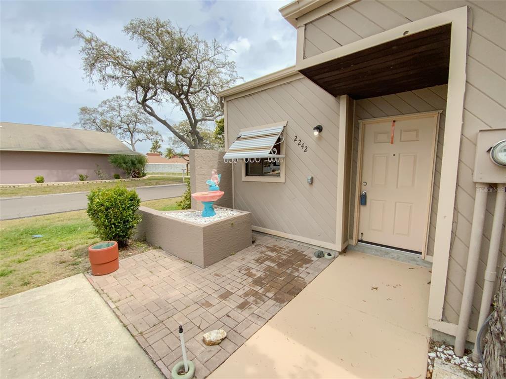 The exterior of a house features a paved walkway, a small fountain, and a front door — 2242 PINEWOOD VILLAS DRIVE, HOLIDAY, FL