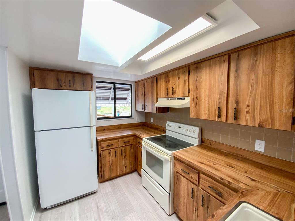A kitchen features wood-grain cabinets, light-colored countertops, a white refrigerator, and a large skylight — 2242 PINEWOOD VILLAS DRIVE, HOLIDAY, FL