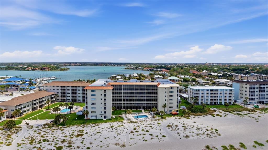 An aerial view shows beachfront apartment buildings with swimming pools along a sandy coastline — 1150 TARPON CENTER DRIVE UNIT 304, VENICE, FL