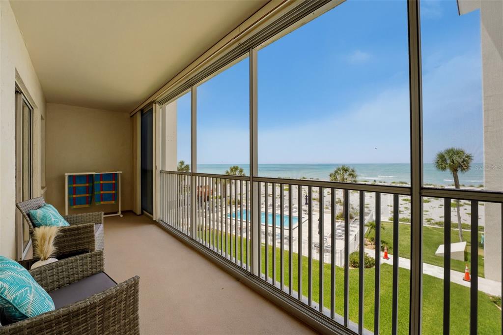 A screened-in balcony with wicker chairs overlooks a swimming pool, lawn, and the ocean — 1150 TARPON CENTER DRIVE UNIT 304, VENICE, FL