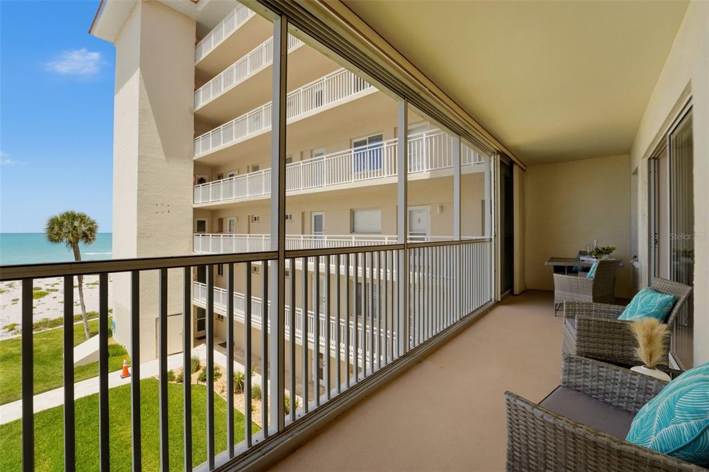 A screened-in balcony features wicker chairs, a small table, and views of the beach — 1150 TARPON CENTER DRIVE UNIT 304, VENICE, FL