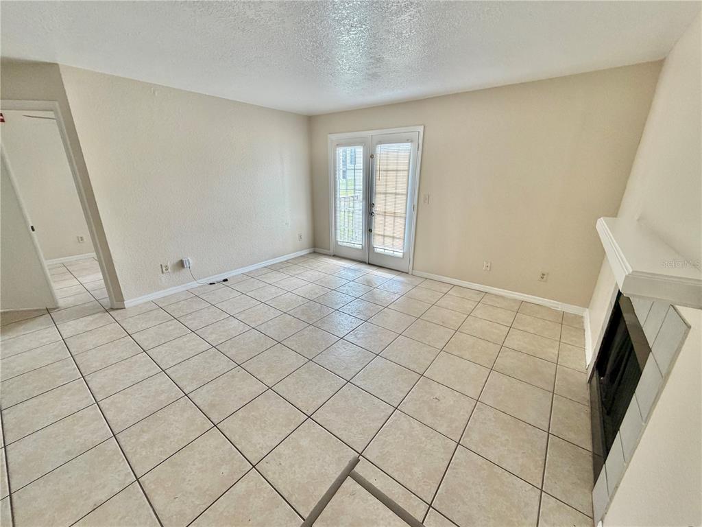 An empty living room features beige tile flooring, a fireplace, and glass French doors — 2550 N ALAFAYA TRAIL UNIT 3103, ORLANDO, FL