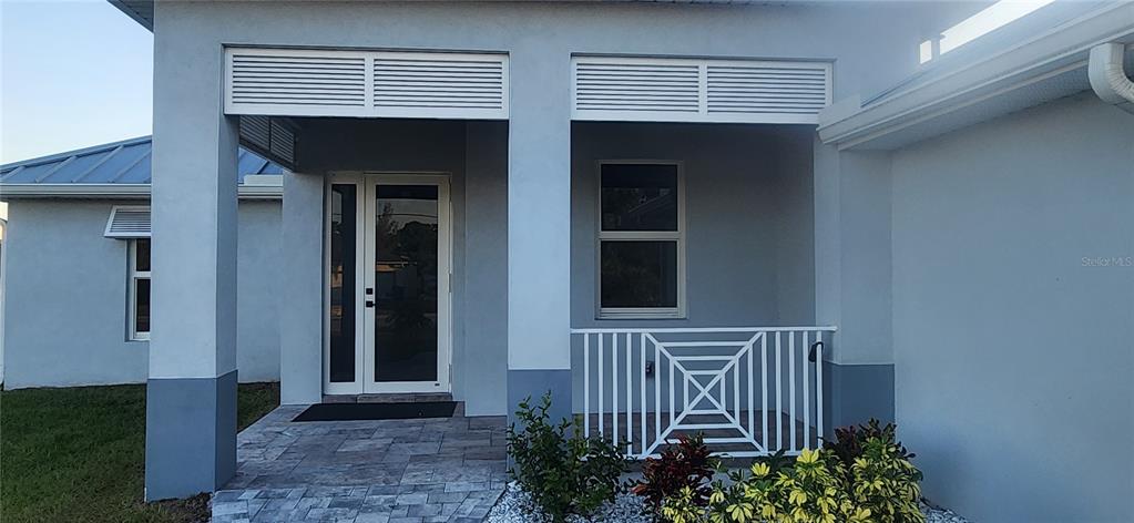 A single-story house with a light gray metal roof, white stucco walls, and a paver driveway — 15267 APPLETON BOULEVARD, PORT CHARLOTTE, FL