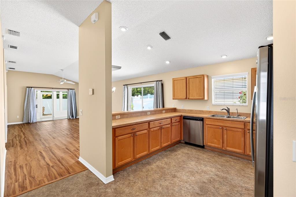 A kitchen with wood cabinets and a stainless steel dishwasher opens to a living area — 430 CALVERT TERRACE, THE VILLAGES, FL