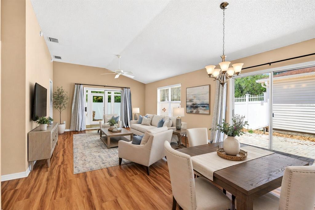 A living and dining area with wood floors, vaulted ceilings, and sliding glass patio doors — 430 CALVERT TERRACE, THE VILLAGES, FL