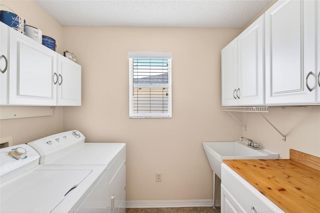 A laundry room features white cabinets, a utility sink, a wooden countertop, and white appliances — 430 CALVERT TERRACE, THE VILLAGES, FL