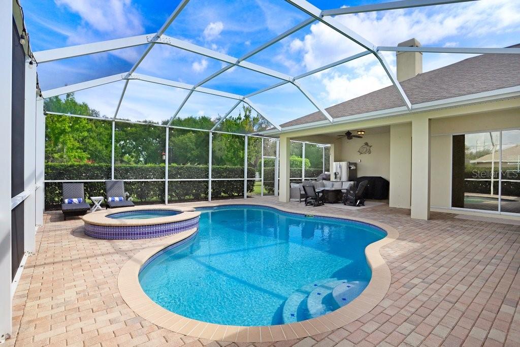 A screened-in patio features a swimming pool, a raised spa, and a covered seating area — 7709 KENIA MEADOWS LANE, ODESSA, FL