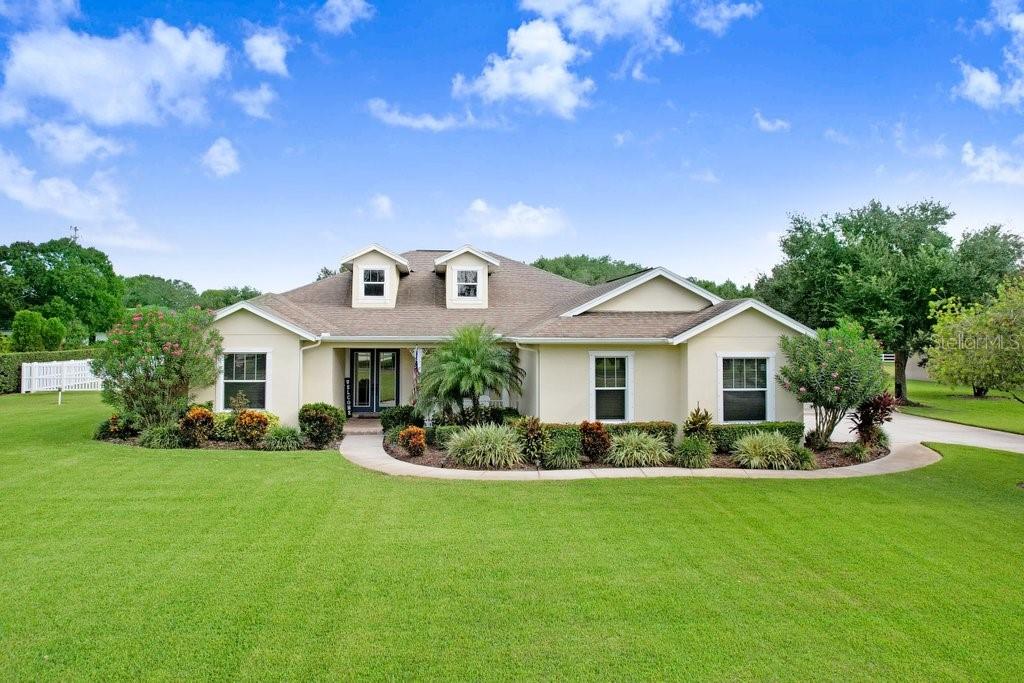 A single-story house with a tan exterior, a brown roof, and a large front lawn — 7709 KENIA MEADOWS LANE, ODESSA, FL