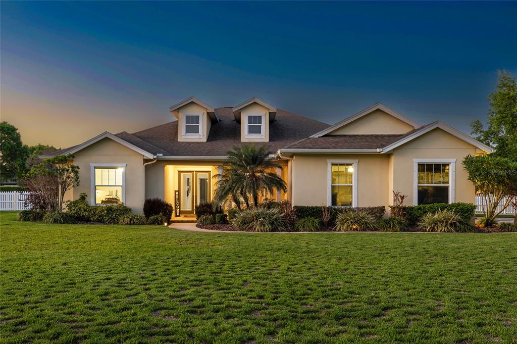 A single-story house with a tan stucco exterior, two dormer windows, and a front lawn — 7709 KENIA MEADOWS LANE, ODESSA, FL