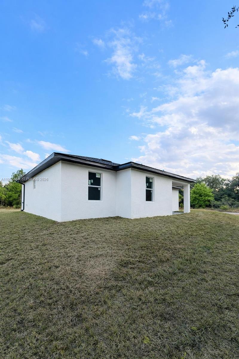 The exterior of a white, single-story house with a dark roof sits on a grassy lot — 3901 E 19th St, Lehigh Acres FL 33972, LEHIGH ACRES, FL