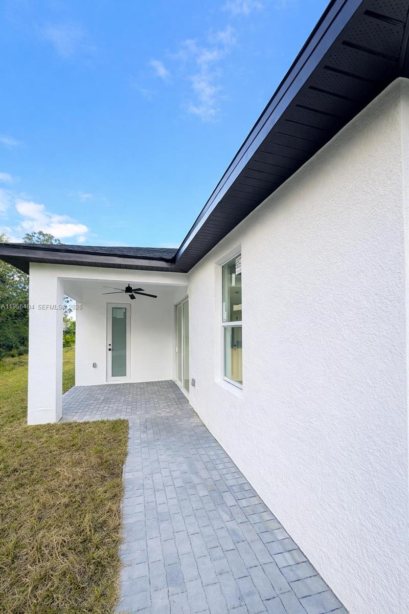 A covered patio with a ceiling fan and paver flooring sits beside a white house — 3901 E 19th St, Lehigh Acres FL 33972, LEHIGH ACRES, FL