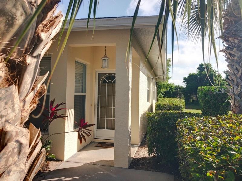 A light-colored house exterior features a covered entryway with a white door and palm trees — 1211 HOT SPRINGS POINT, ENGLEWOOD, FL