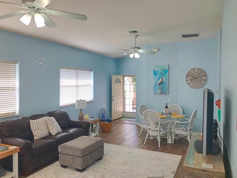 A living room with light blue walls, a dark leather sofa, and a dining area — 1211 HOT SPRINGS POINT, ENGLEWOOD, FL