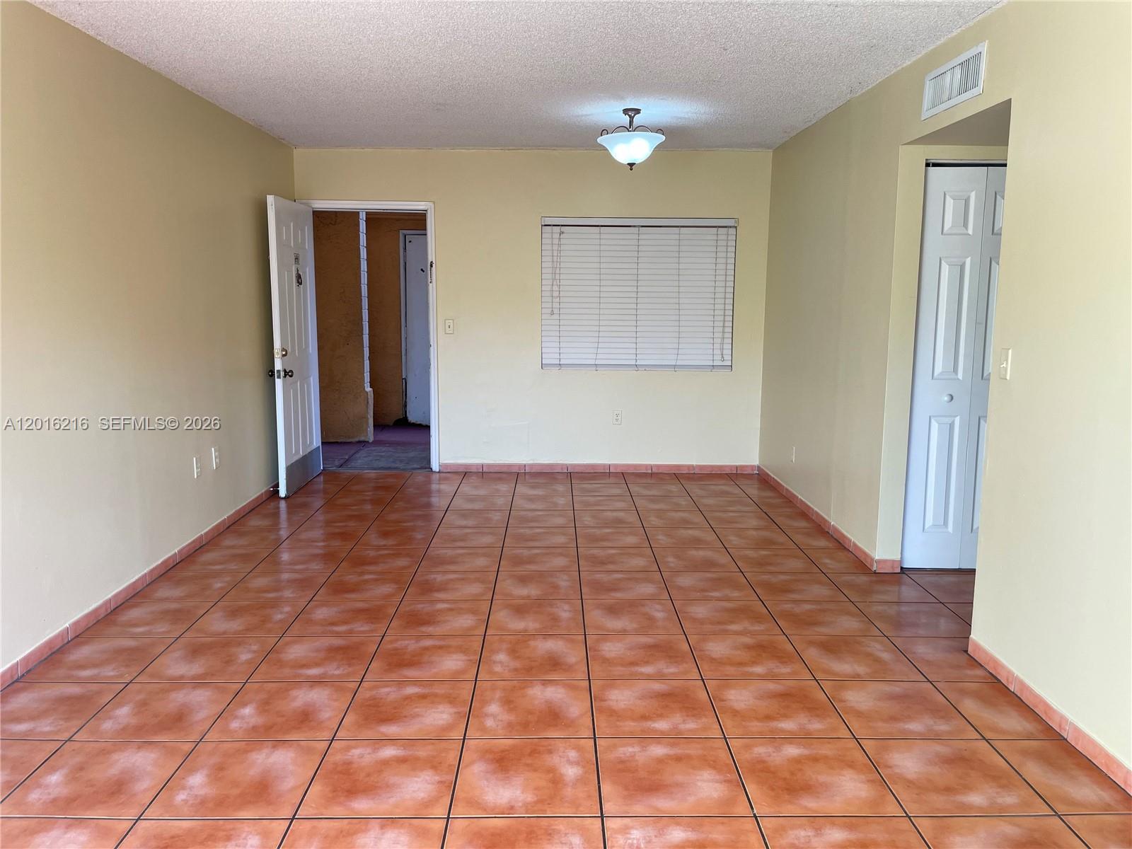 An empty room features tan walls, brown tile flooring, a ceiling light, and white doors — 6255 Kendale Lakes Cir # 116, Miami FL 33183, MIAMI, FL