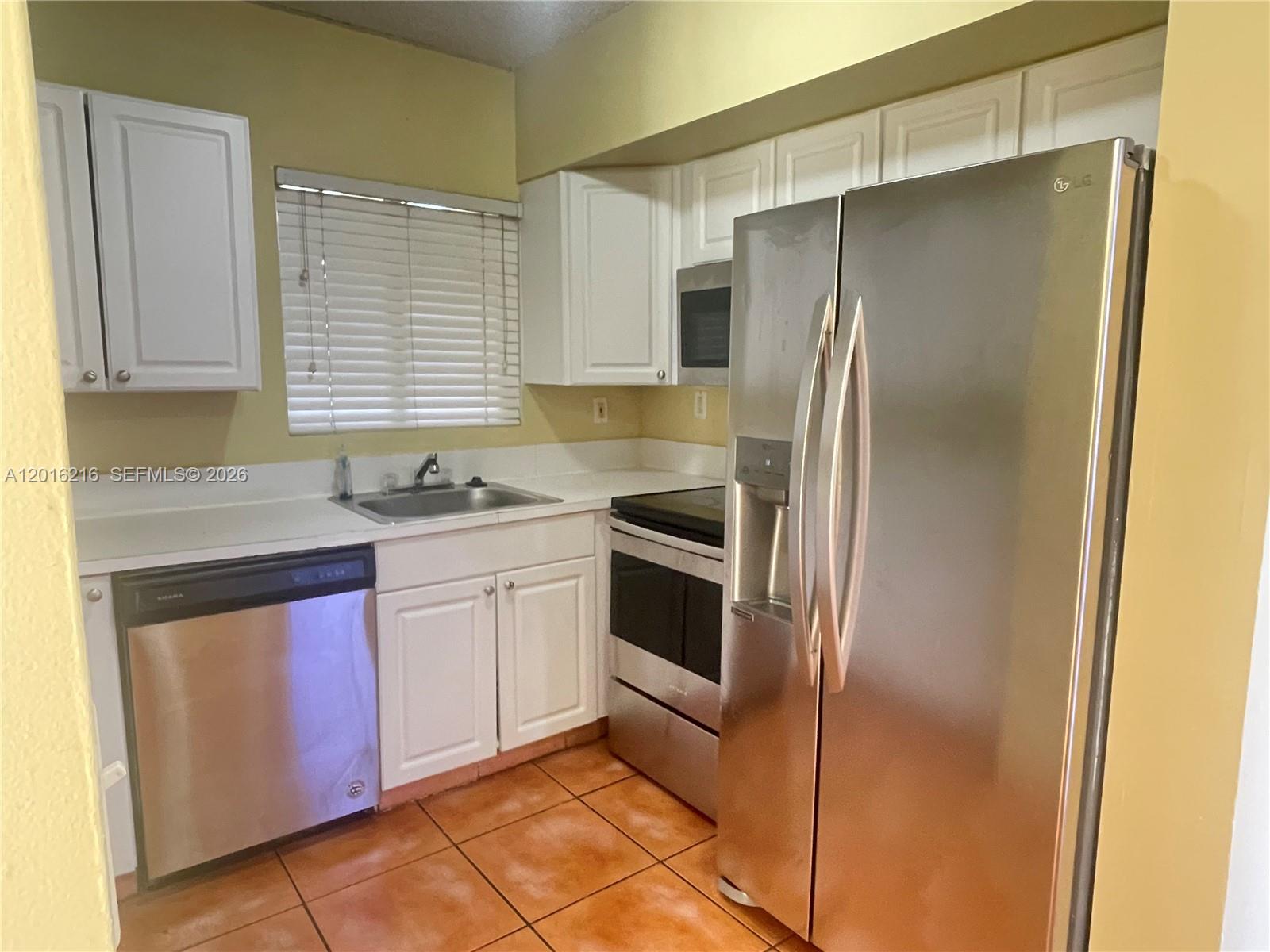 A kitchen features white cabinets, stainless steel appliances, and orange tile flooring — 6255 Kendale Lakes Cir # 116, Miami FL 33183, MIAMI, FL
