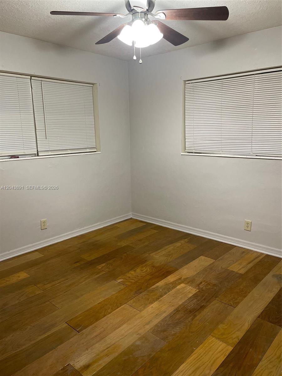 An empty room features light gray walls, wood-look flooring, two windows with blinds, and a ceiling fan — WEST PARK, FL