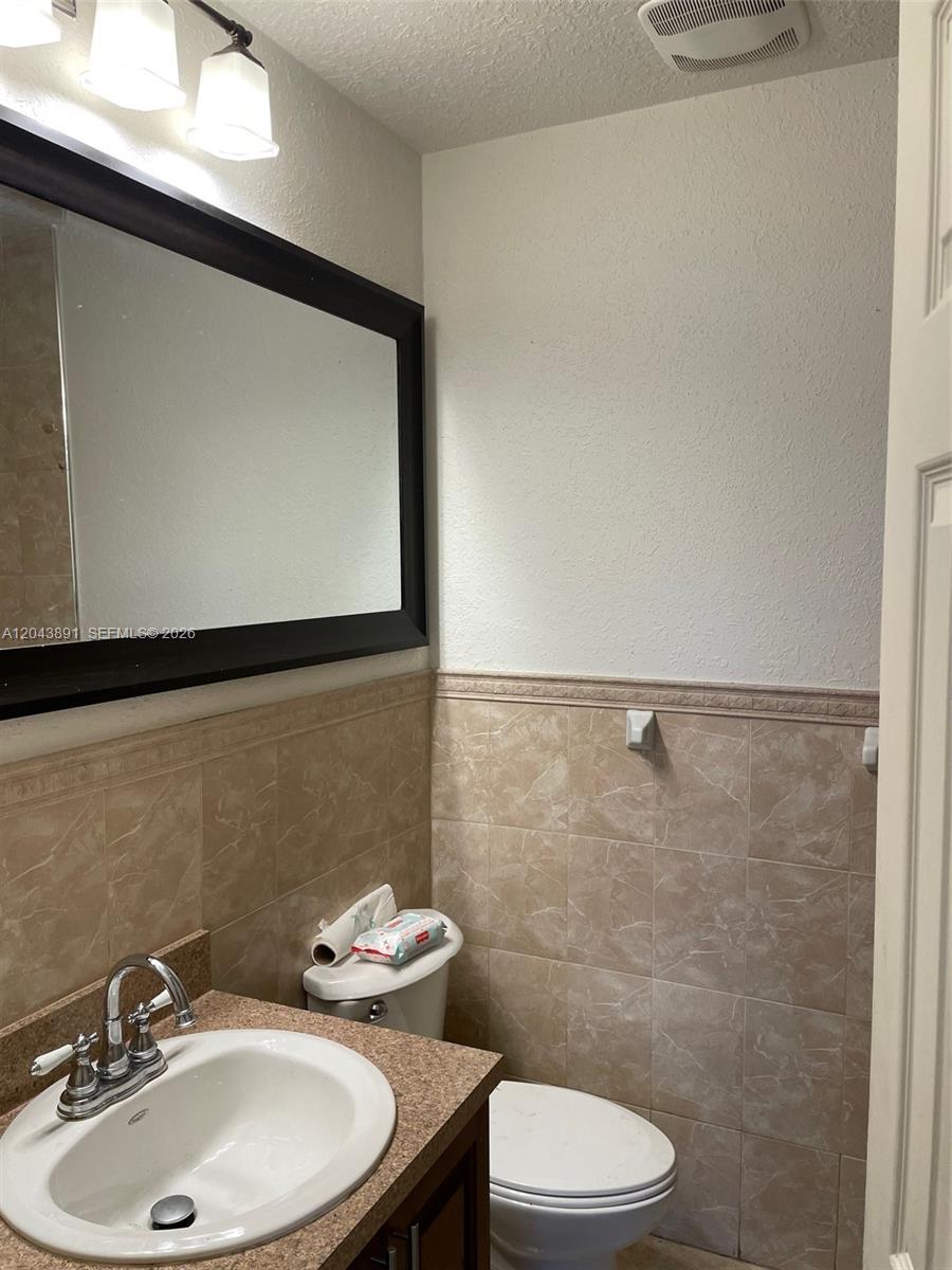 A bathroom features a vanity with a sink, a toilet, and beige tiled walls — WEST PARK, FL