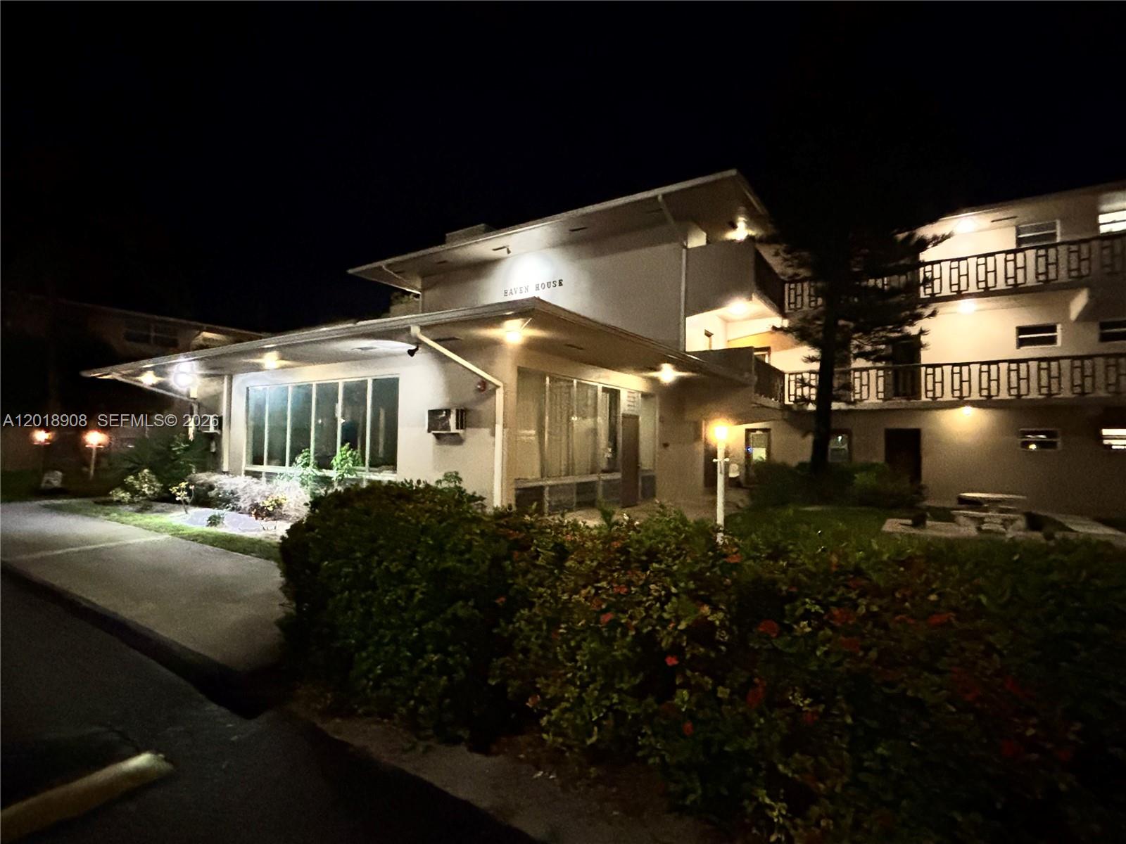 A multi-story apartment building exterior is illuminated at night with landscaping in the foreground — 1480 E Sample Rd # 209, Pompano Beach FL 33064, POMPANO BEACH, FL