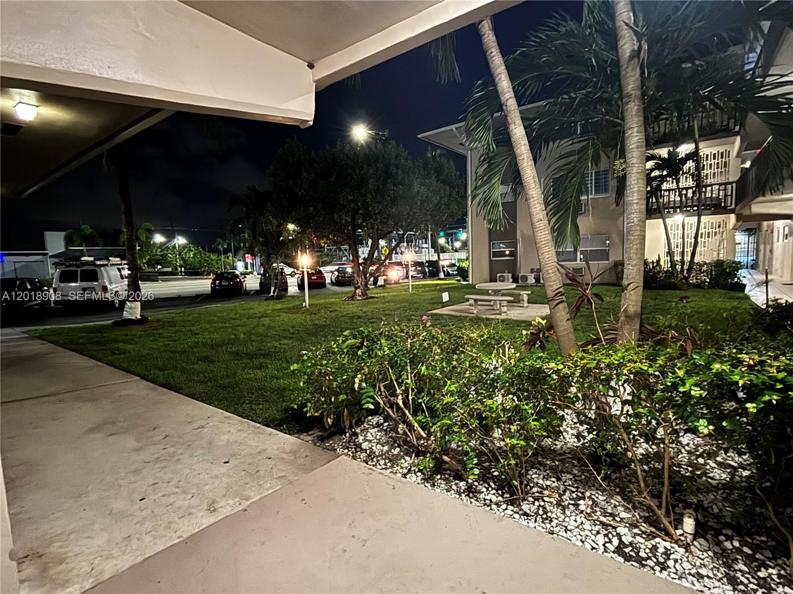A night view of a residential building exterior with a lawn, palm trees, and parking — 1480 E Sample Rd # 209, Pompano Beach FL 33064, POMPANO BEACH, FL