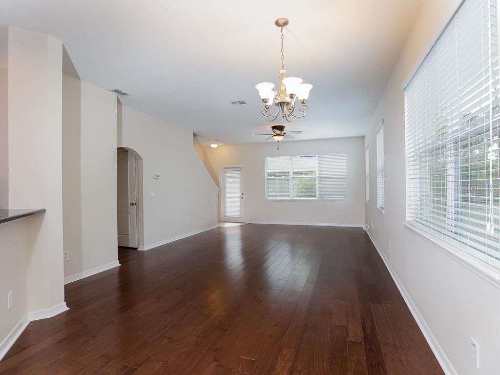An empty living room features dark hardwood floors, a chandelier, and large windows with blinds — 12230 LANGSTAFF DRIVE, WINDERMERE, FL