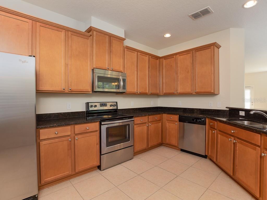 A kitchen with light wood cabinets, dark granite countertops, and stainless steel appliances — 12230 LANGSTAFF DRIVE, WINDERMERE, FL