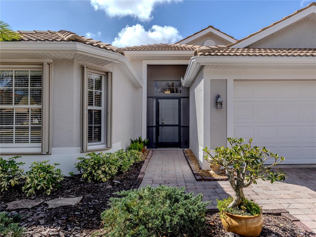 The exterior of a house features a paved walkway leading to a front door with a screen — 11500 DANCING RIVER DRIVE, VENICE, FL