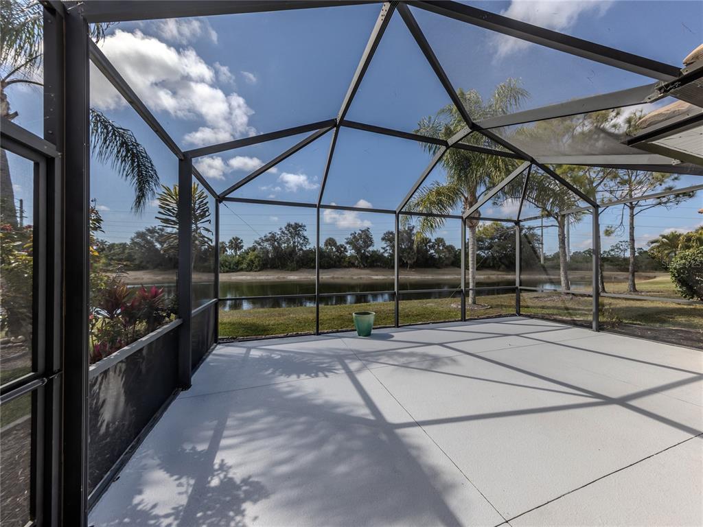A screened-in patio with a concrete floor overlooks a lake and palm trees — 11500 DANCING RIVER DRIVE, VENICE, FL