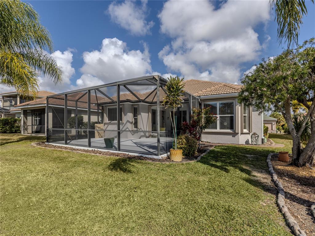 A house exterior features a screened-in patio, a tiled roof, and a grassy backyard — 11500 DANCING RIVER DRIVE, VENICE, FL