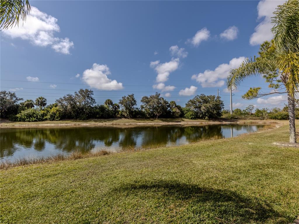 A grassy lawn slopes down to a pond bordered by trees under a blue sky — 11500 DANCING RIVER DRIVE, VENICE, FL