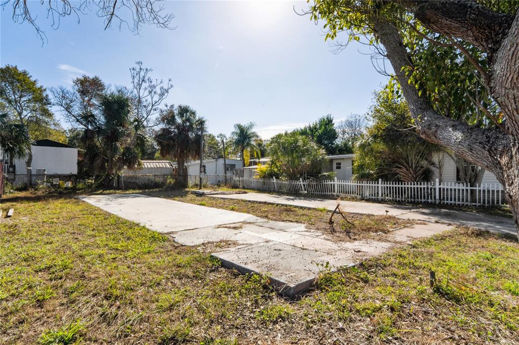 A vacant lot features a concrete slab foundation surrounded by grass, trees, and a fence — 736 DRIFTWOOD LANE, TARPON SPRINGS, FL