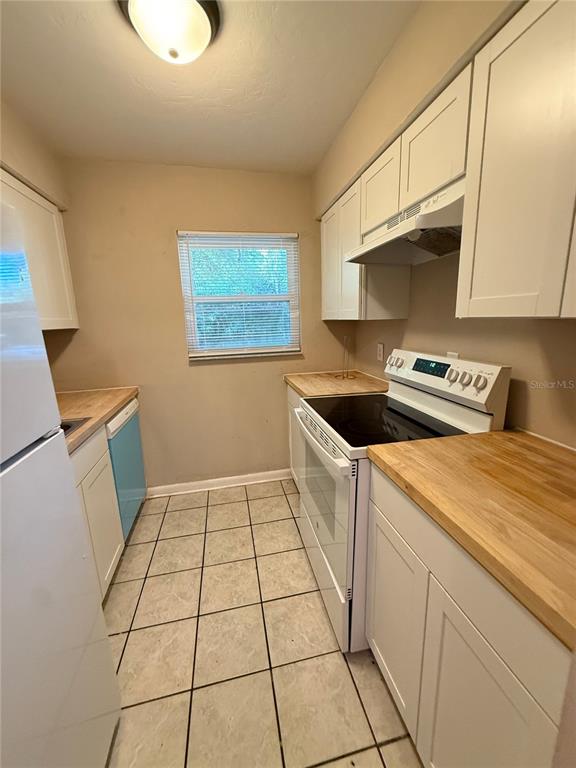 A galley kitchen features white cabinets, light wood countertops, a white stove, and tiled flooring — 1721 SW 68TH TERRACE UNIT 1721, GAINESVILLE, FL