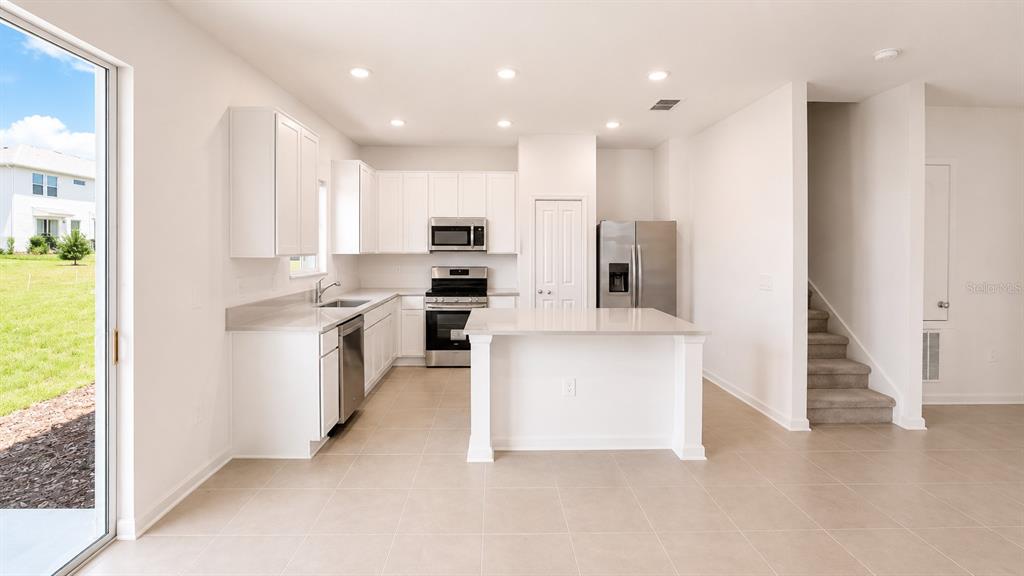 A modern kitchen features white cabinets, stainless steel appliances, a center island, and tile flooring — 6069 ZEN WAY, CLERMONT, FL