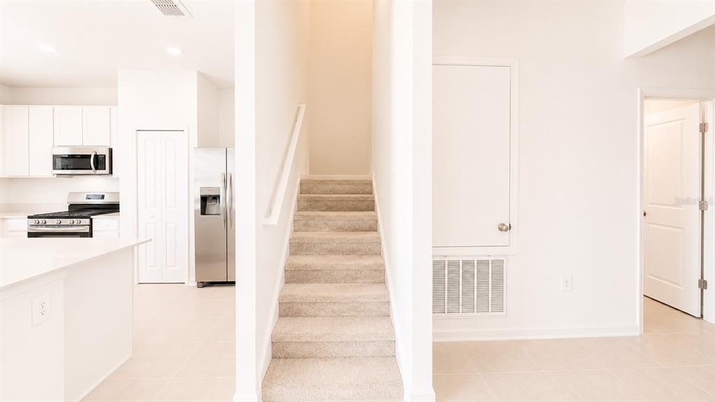A kitchen with stainless steel appliances sits beside a carpeted staircase and a closed door — 6069 ZEN WAY, CLERMONT, FL