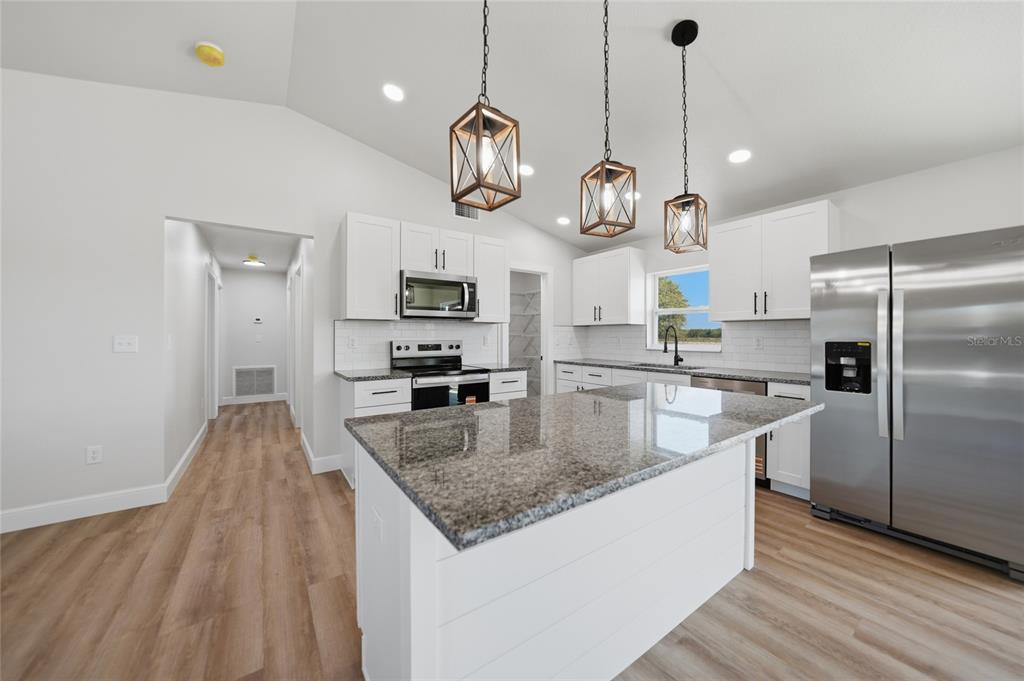 A modern kitchen features white cabinets, granite countertops, a center island, and stainless steel appliances — 6894 SW MIAMI AVENUE, ARCADIA, FL