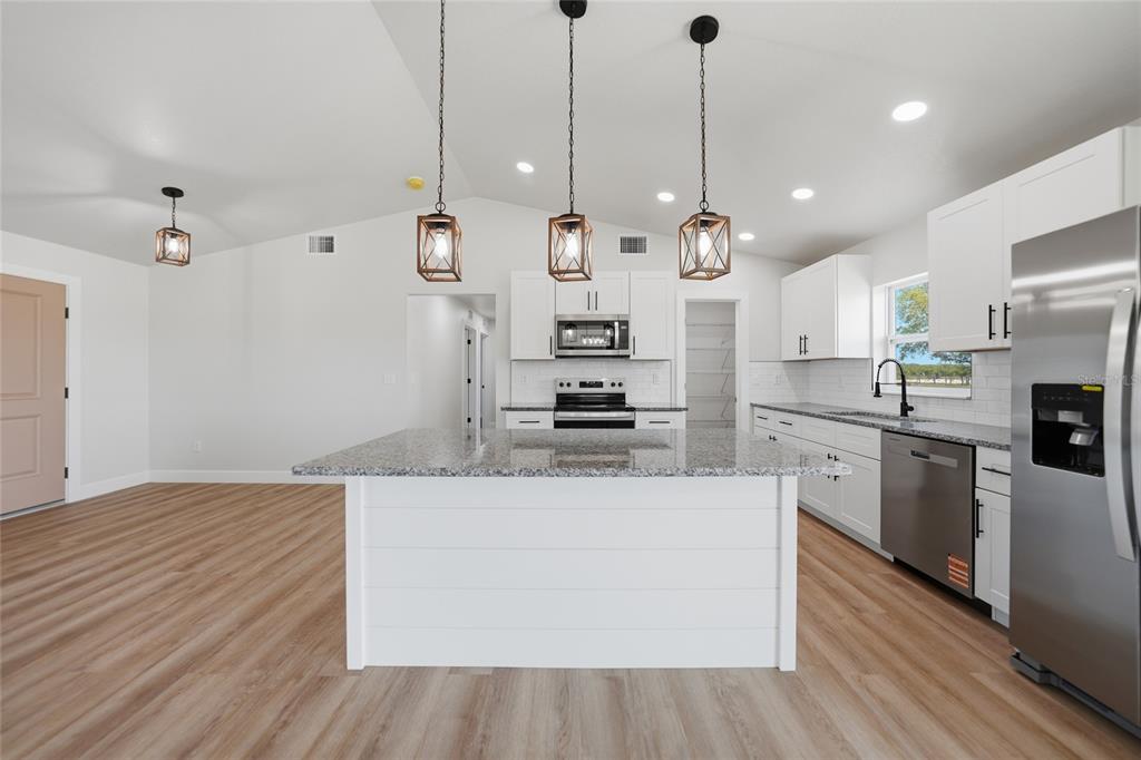 A modern kitchen features white cabinets, granite countertops, a central island, and stainless steel appliances — 6894 SW MIAMI AVENUE, ARCADIA, FL