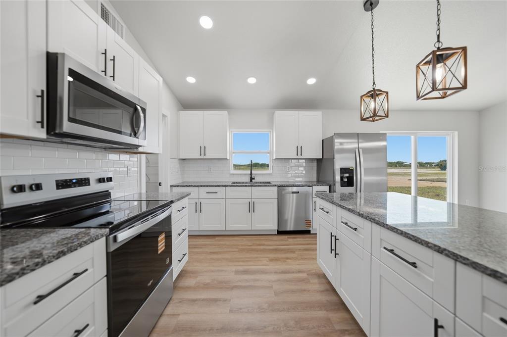 A modern kitchen features white cabinets, granite countertops, stainless steel appliances, and wood-look flooring — 6894 SW MIAMI AVENUE, ARCADIA, FL