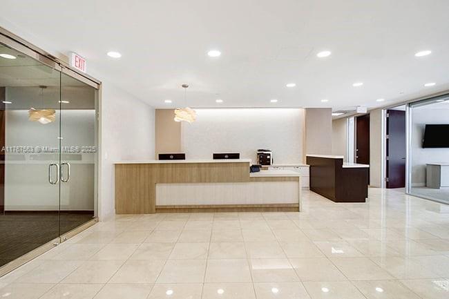 A modern office reception area features a long wooden desk, tile flooring, and glass doors — 100 SE 2 ST # 2000, Miami FL 33131, MIAMI, FL