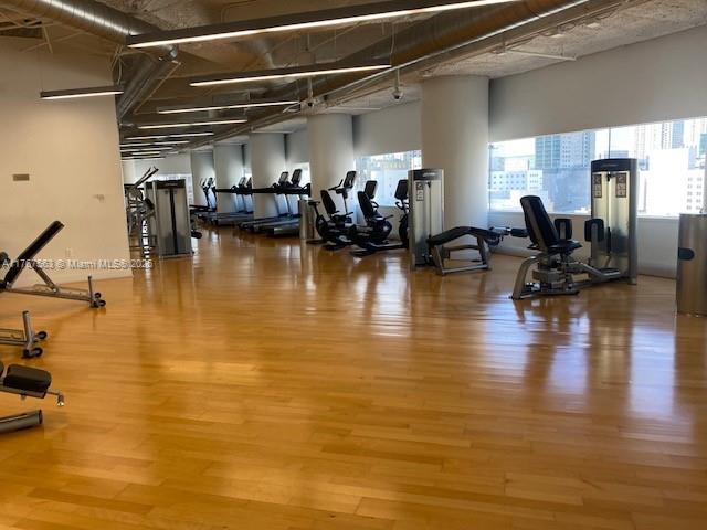 A gym features various exercise machines, light wood flooring, and exposed industrial ceiling fixtures — 100 SE 2 ST # 2000, Miami FL 33131, MIAMI, FL